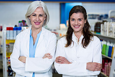 Portrait of smiling pharmacists standing with arms crossed in pharmacy